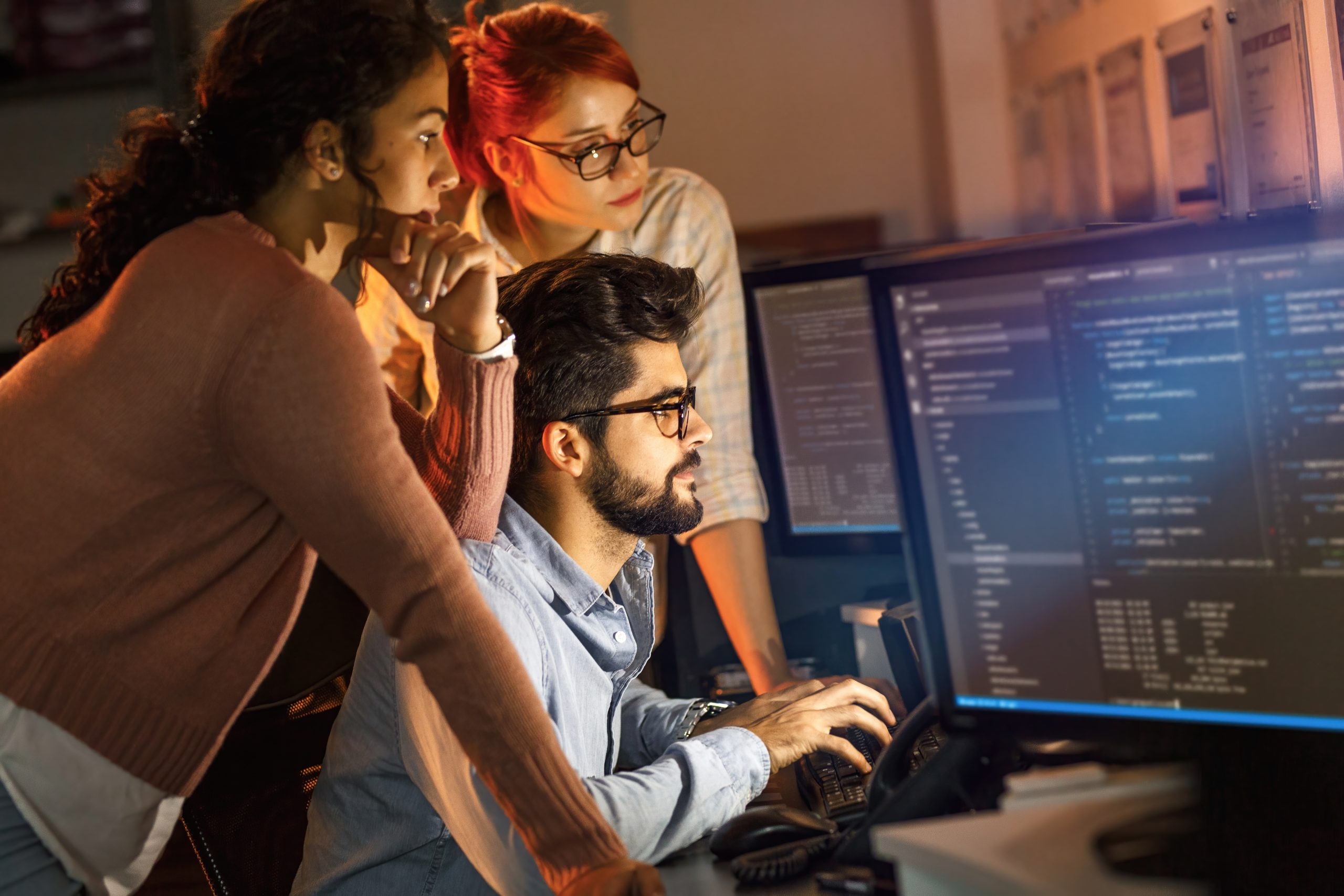 Duas mulheres e um rapaz trabalhando com programação.